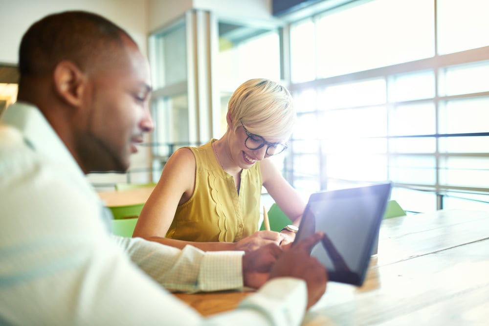 Two creative millenial small business owners working on social media strategy using a digital tablet while sitting at desk