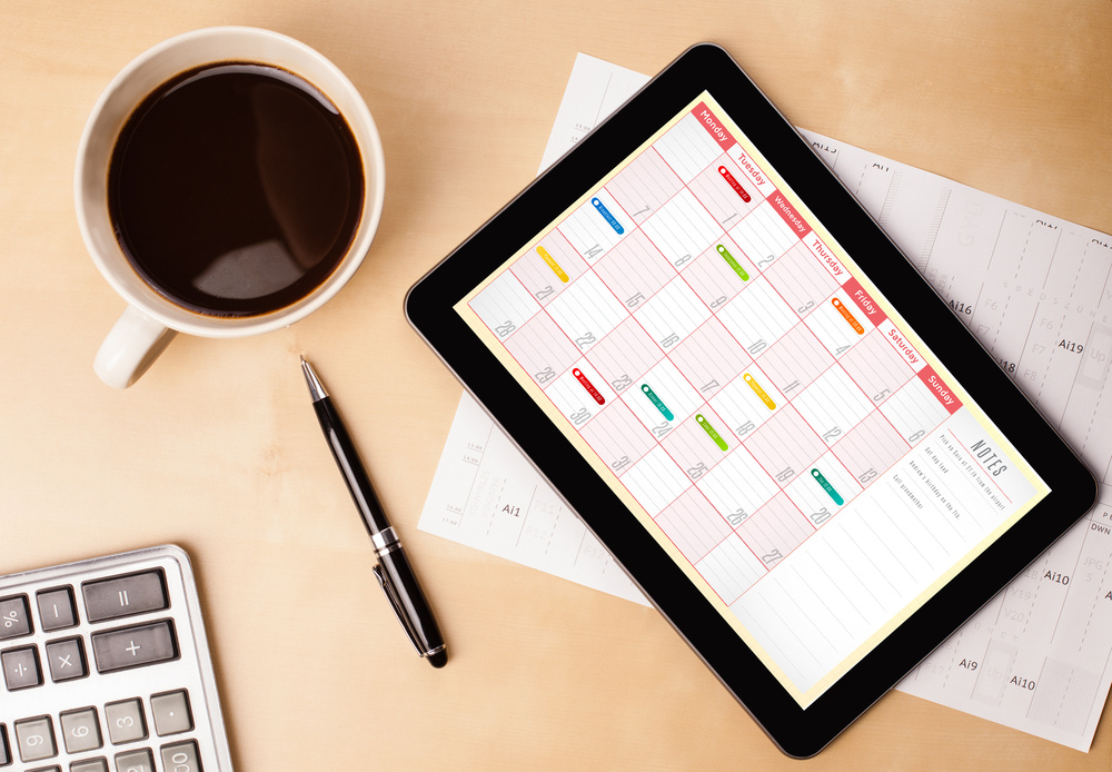 Workplace with tablet pc showing calendar and a cup of coffee on a wooden work table close-up