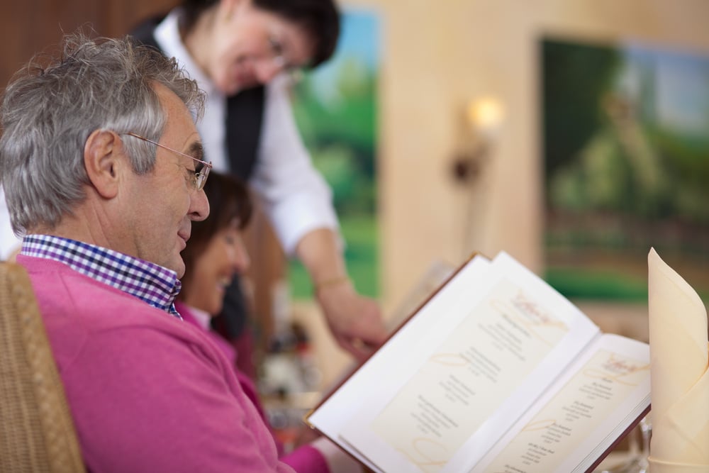 smiling guest in restaurant reading the menu with waitress in background